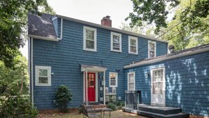 A two-story blue house with a red front door, a small porch, and a brick chimney. - Colorful Downtown Historic 2BR Shingle Home (Spartanburg)