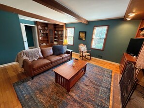 A living room with a brown leather sofa, a wooden coffee table, a patterned rug, a bookshelf, and a fireplace.