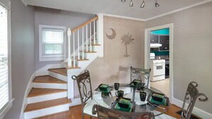 A dining area with a round table, chairs, and a staircase leading to another room. - Colorful Downtown Historic 2BR Shingle Home (Spartanburg)