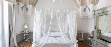 A four-poster canopy bed with a white canopy, a chandelier, and a mirror above it.