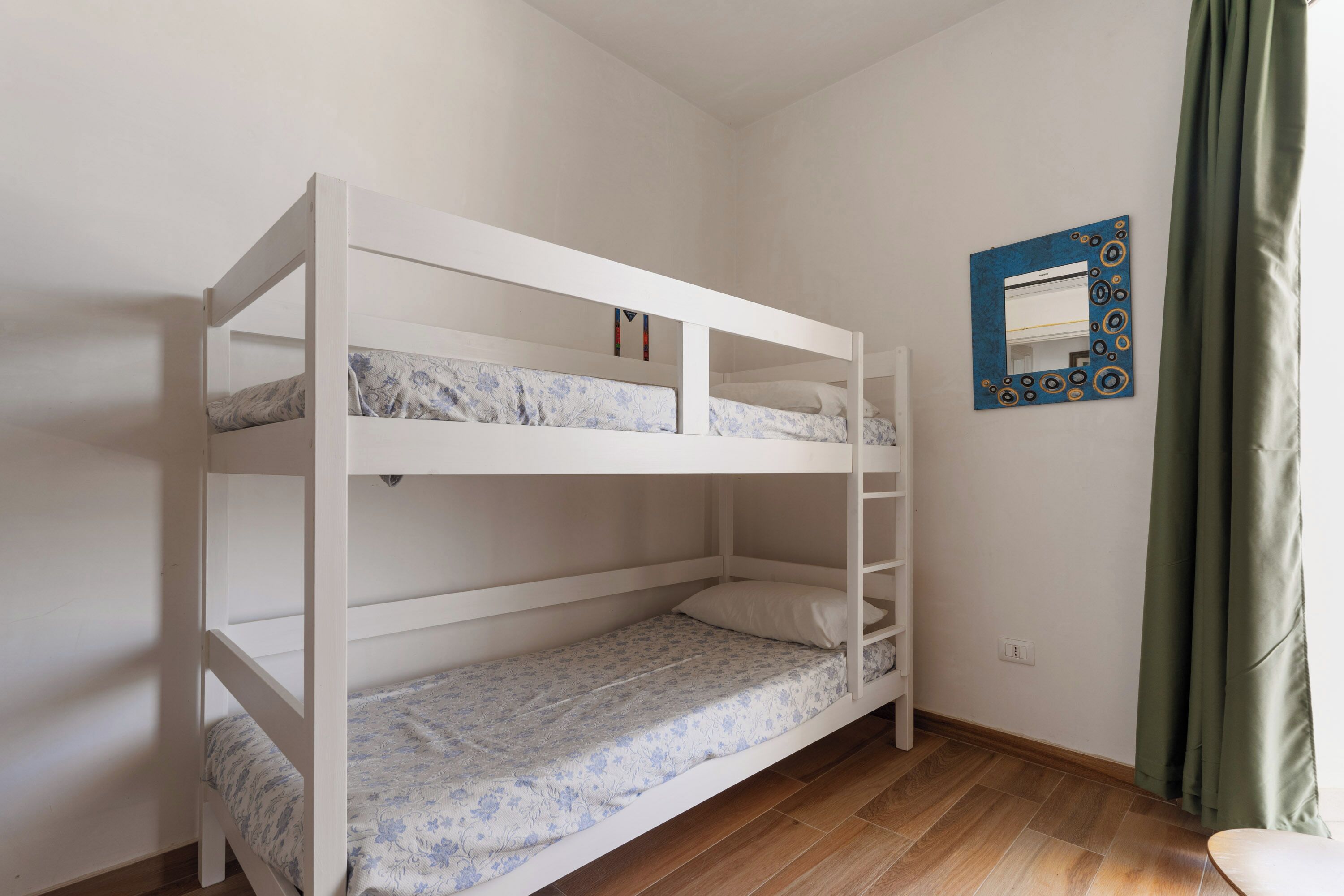 A bunk bed with a lower bunk and a top bunk, a mirror with a decorative frame, and a green curtain.