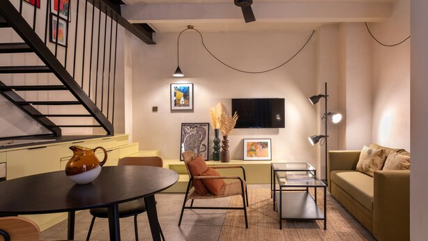 Ein modernes Wohnzimmer mit Treppe, Flachbildfernseher, Esstisch und Sofa.