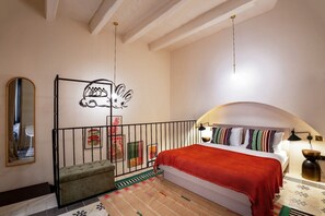 A bedroom with a bed, a small seating area, a mirror, and artwork on the walls.