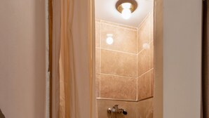 Eine Dusche mit Duschbrause, Wandleuchte und Fliesenboden.