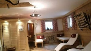 Una habitación acogedora con paredes de madera, una mesa de comedor, dos sillones y un ventanal con cortinas.