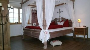 Una cama con dosel y cortinas blancas, cabecera de madera y ropa de cama roja.