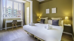 Et hotelværelse med en stor seng, to sengeborde med lamper, et skrivebord med stol og et vindue med gardiner.