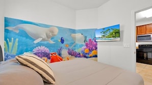 A bedroom with a mural of marine life, a bed with pillows, and a view of a kitchen. - Pretty & Welcoming Resort Condo (Kissimmee)