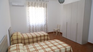 Une chambre avec deux lits, une armoire, une chaise et un rideau.