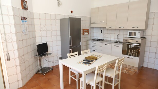 Une cuisine compacte avec des meubles blancs, un réfrigérateur, un four à micro-ondes et une table à manger avec des chaises.