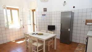 Une cuisine de taille réduite comprenant une table à manger, des chaises, un réfrigérateur et un téléviseur.