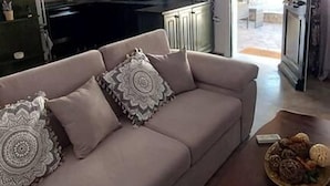 Een woonkamer met een bank, een bijzettafeltje en een keuken op de achtergrond.