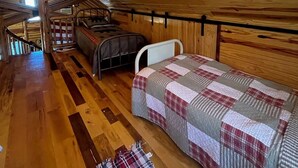 Een gezellig slaapkamer onder het dak, met houten plafond, een stapelbed, een enkel bed en een kleine tafel.