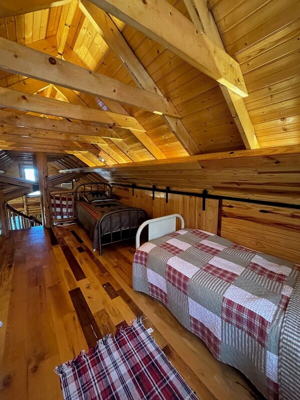 A cozy attic bedroom with a wooden ceiling, a bunk bed, a single bed, and a small table.