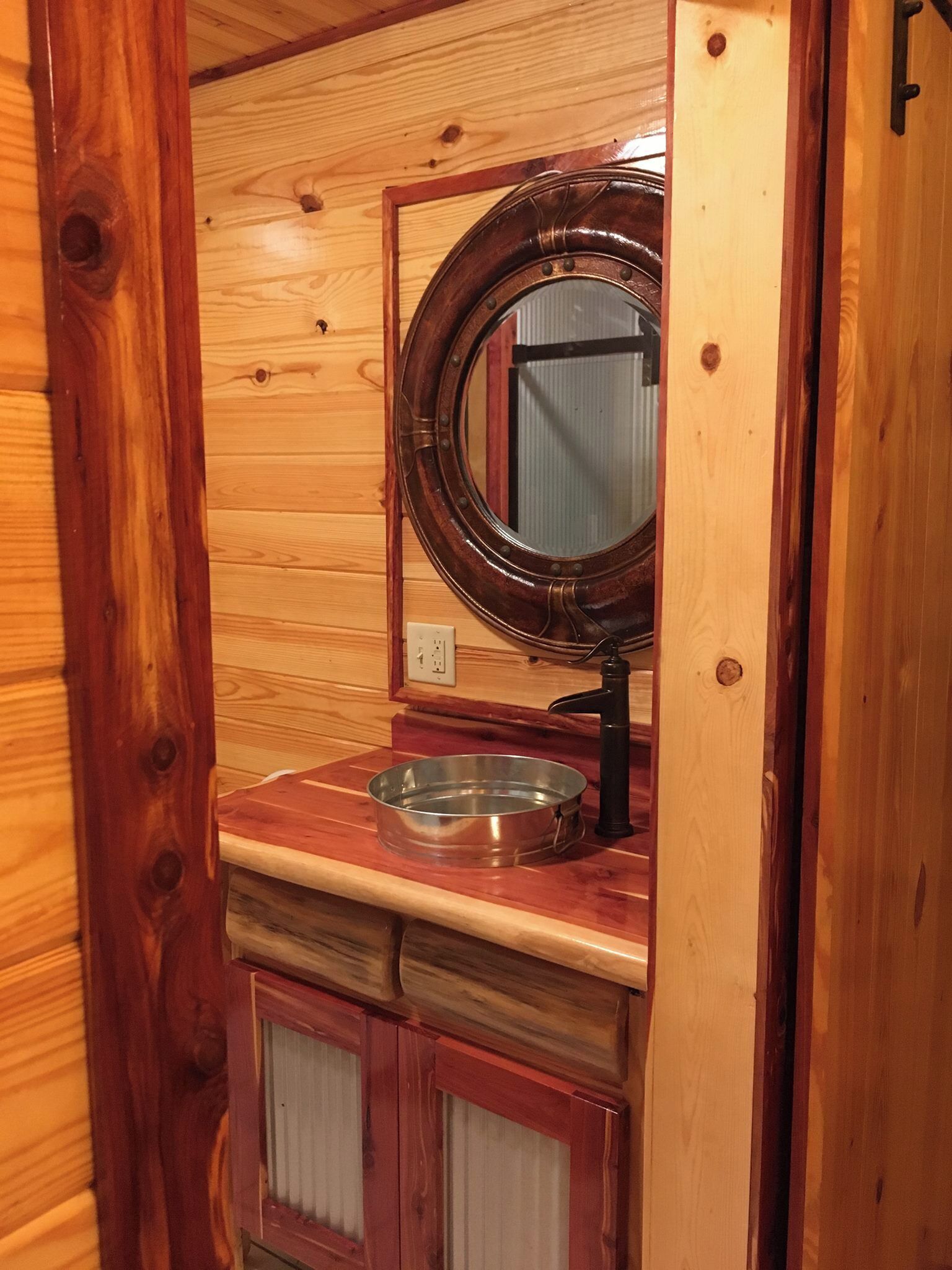 A wooden cabin interior with a round mirror, a metal basin, and wooden cabinets.