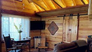 Een gezellige woonkamer met houten plafond, plafondventilator, open haard en een aan de muur bevestigde televisie.