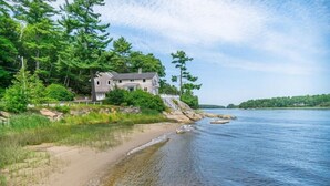 Ein Haus an einem See mit Sandstrand und dichter Baumgrenze.