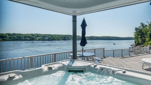 Ein Whirlpool auf einer Terrasse mit Blick auf einen See und Bäume.
