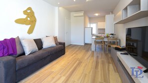 Ein modernes Wohnzimmer mit einer Couch, einem Flachbildfernseher und einer Küche im Hintergrund.