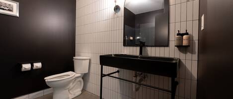 Et moderne badeværelse med en sort vask, hvide fliser, et toilet og et billede i ramme på væggen.