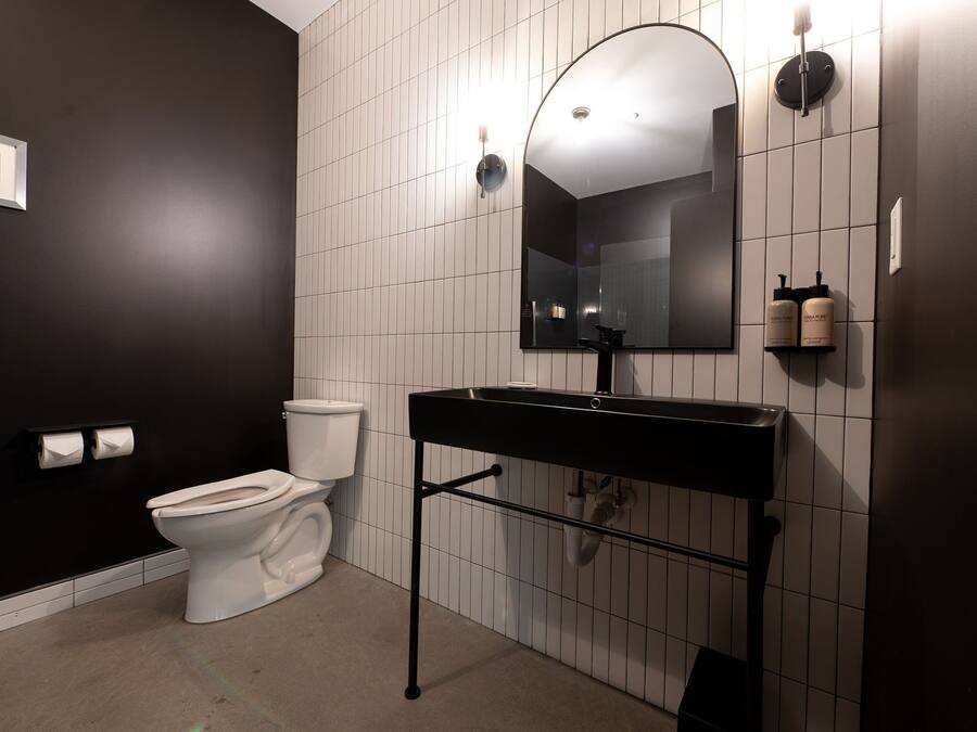 Une salle de bain moderne avec un lavabo noir, des carreaux blancs, des toilettes et un tableau encadré au mur.