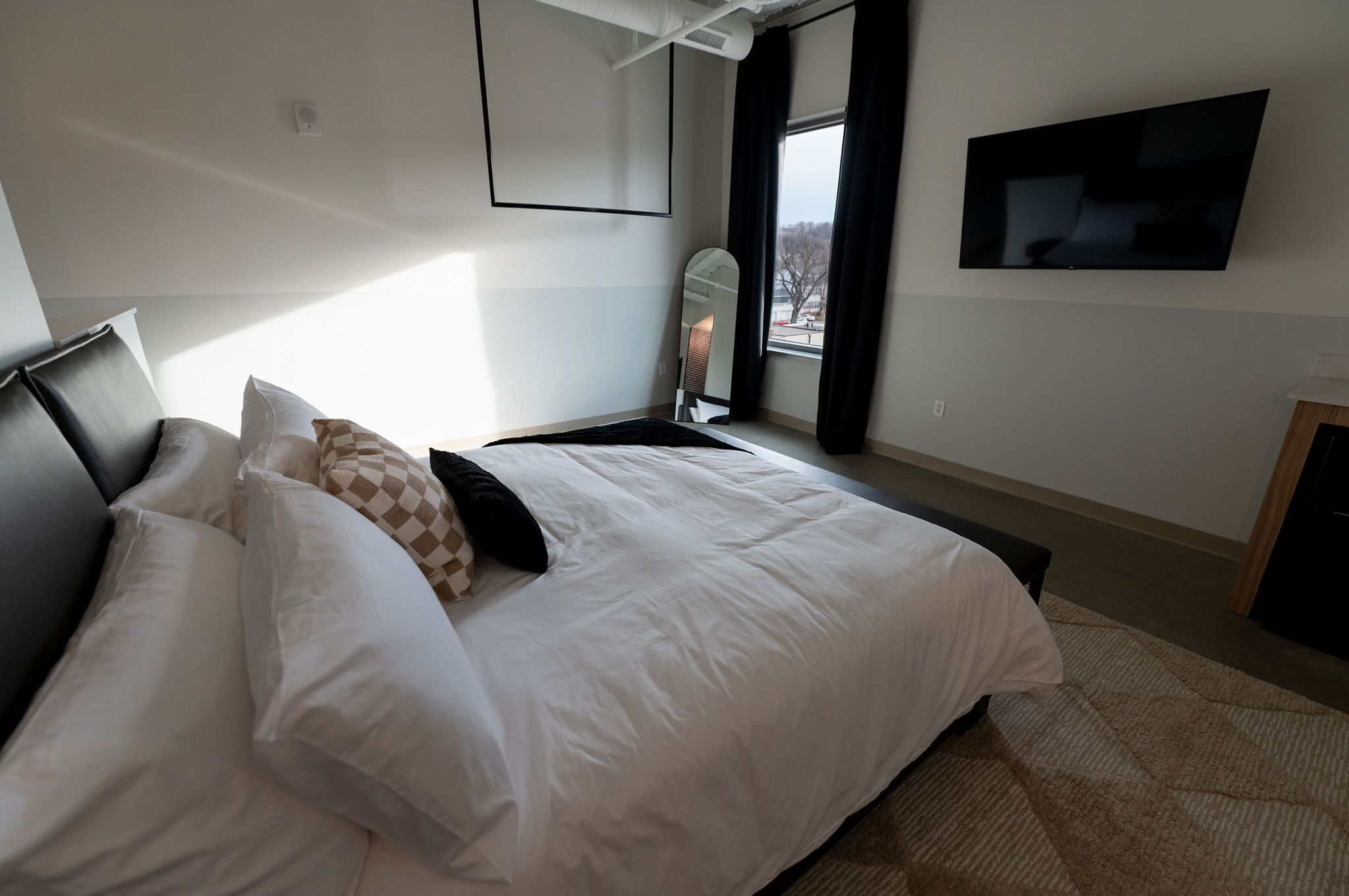 Una camera da letto moderna con un letto grande, una televisione a schermo piatto montata a parete e una finestra con tende.