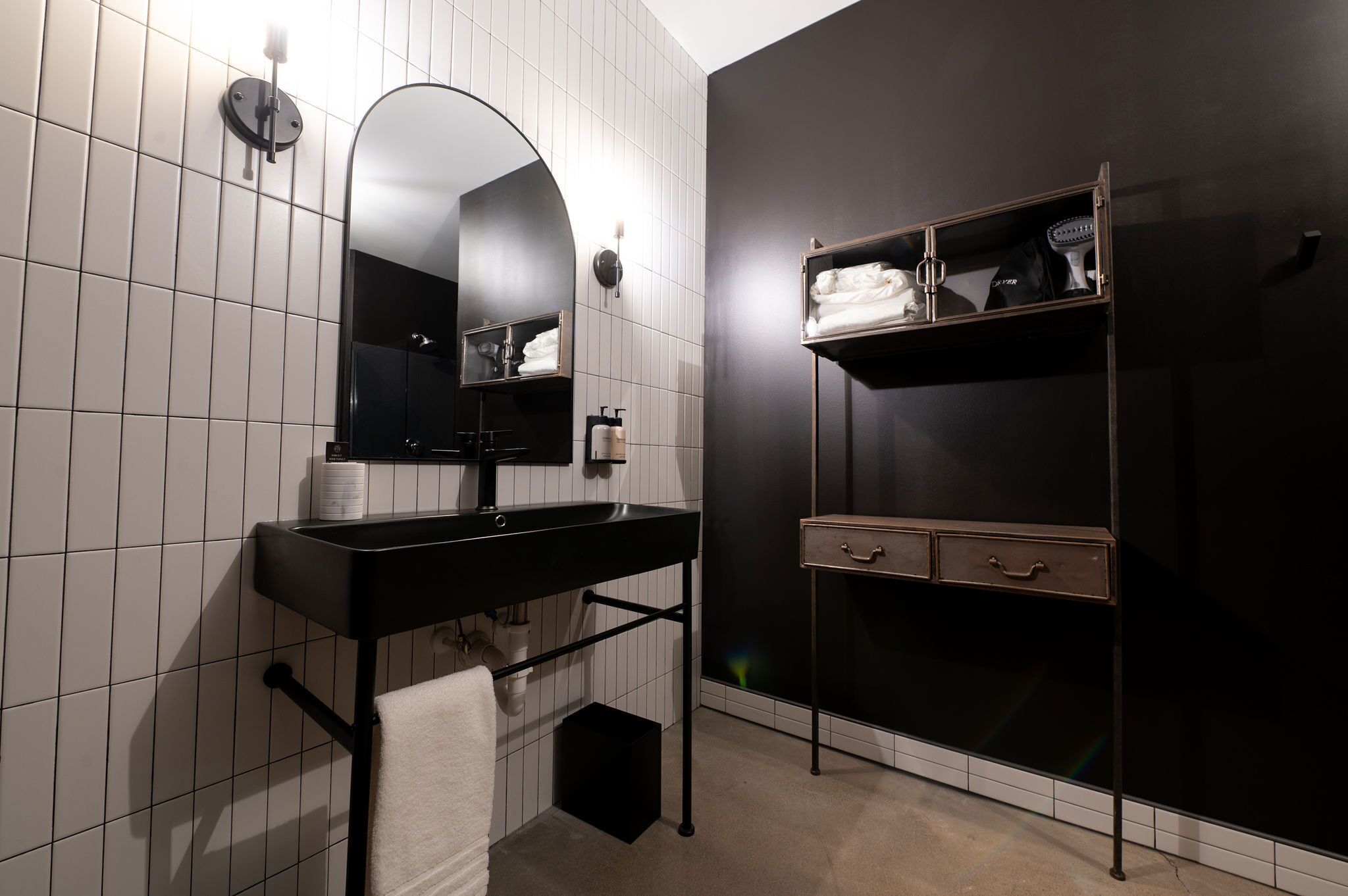 Un baño moderno con un tocador negro, un espejo grande y un estante con artículos de aseo.