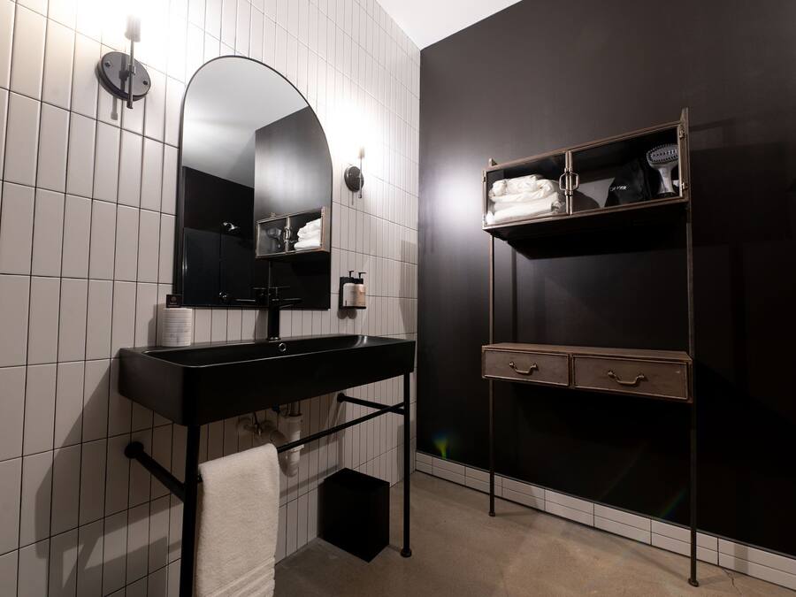 A modern bathroom with a black vanity, a large mirror, and a shelf with toiletries.