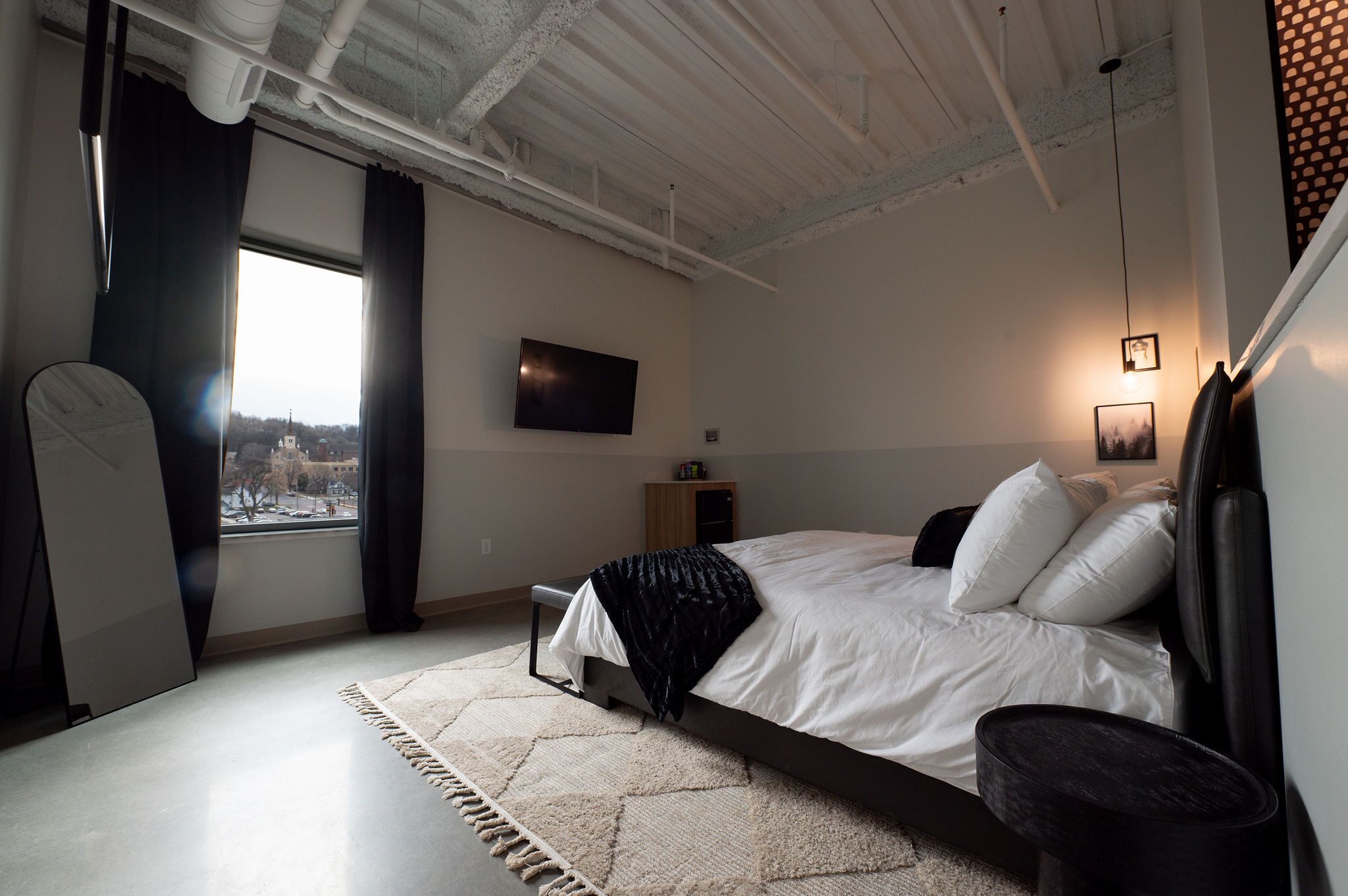 A bedroom with a bed, a desk, a chair, a TV, and a window with curtains.