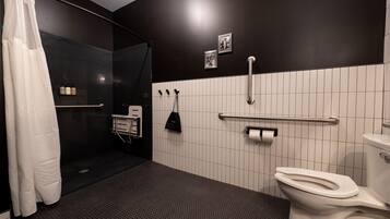 A modern bathroom with a shower, toilet, and handrails.