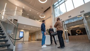 Een moderne hotellobby met een glazen trap, een receptiebalie en een groot raam.