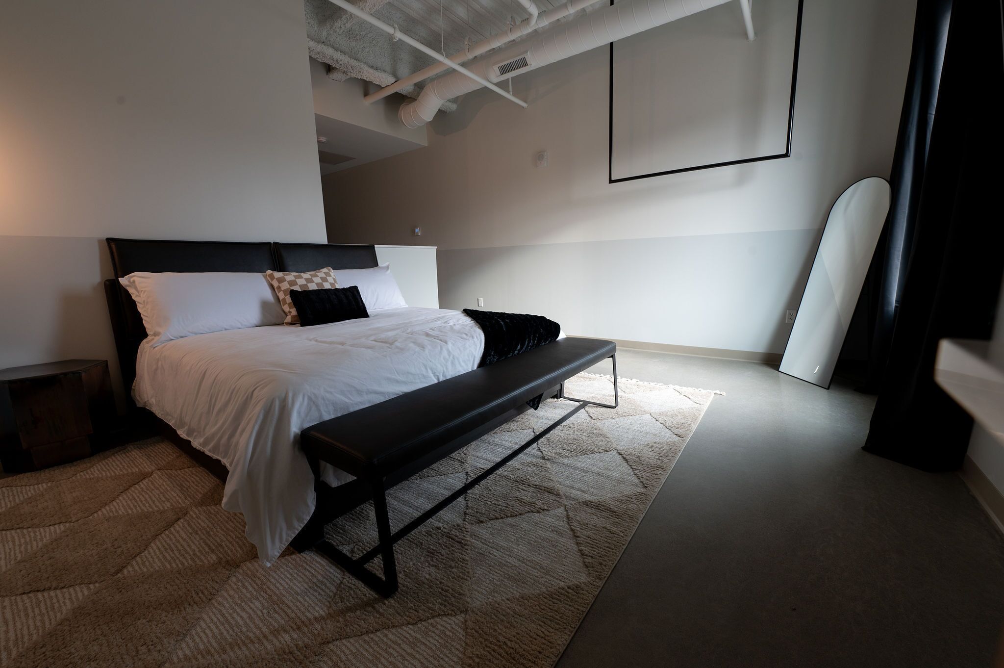 Un dormitorio moderno con una cama, un banco y una tabla de surf apoyada en la pared.