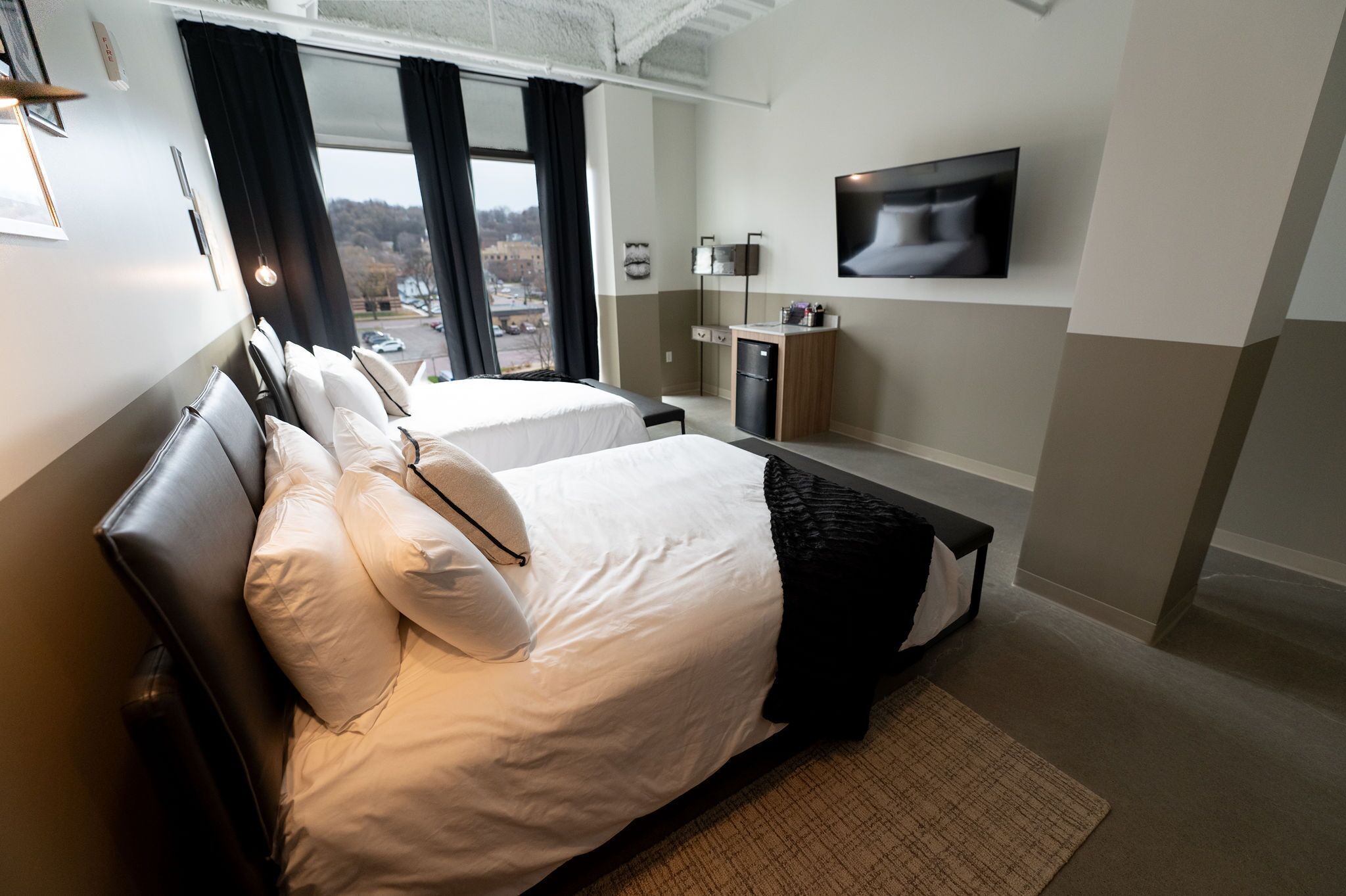 Ein Hotelzimmer mit zwei Betten, einem Fernseher, einer kleinen Küchenzeile und Blick auf die Stadt.