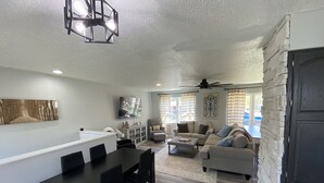 Ein modernes Wohnzimmer mit Essbereich, einem an der Wand befestigten Flachbildfernseher und einem Deckenventilator.