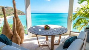 A round wooden table with a fruit bowl and glasses, overlooking a beach and turquoise sea. - Tamarind Hills Resort - Ocean Azul (Antigua and Barbuda)