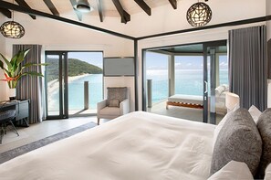 Un dormitorio moderno con una cama grande, un escritorio y una silla. Cuenta con una puerta de cristal corredera que da a un balcón con vistas al océano.