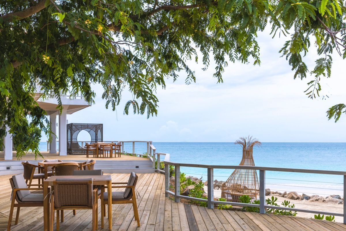 Eine Holzterrasse mit Sitzgelegenheiten mit Blick auf einen Strand.