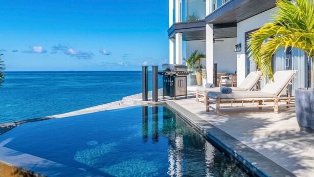 A modern infinity pool with a clear view of the ocean, a barbecue grill, and lounge chairs on a terrace. - Tamarind Hills Resort - Ocean Azul (Antigua and Barbuda)