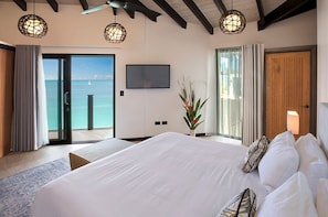 Habitación de hotel con una cama grande, televisión, planta y vista al mar a través de una puerta corrediza.