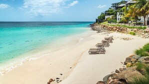 A beach with lounge chairs lined up, a rocky shoreline, and a building with a balcony overlooking the ocean. - Tamarind Hills Resort - Ocean Blessed (Antigua and Barbuda)