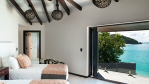 A bedroom with two beds, a large sliding glass door to a balcony, and a view of the sea. - Tamarind Hills Resort - Ocean Blessed (Antigua and Barbuda)