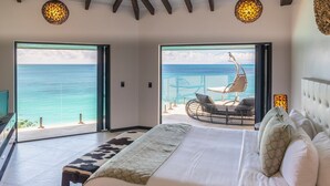 A bedroom with a large bed, a view of the ocean, and a seating area with a chair and table. - Tamarind Hills Resort - Ocean Blessed (Antigua and Barbuda)