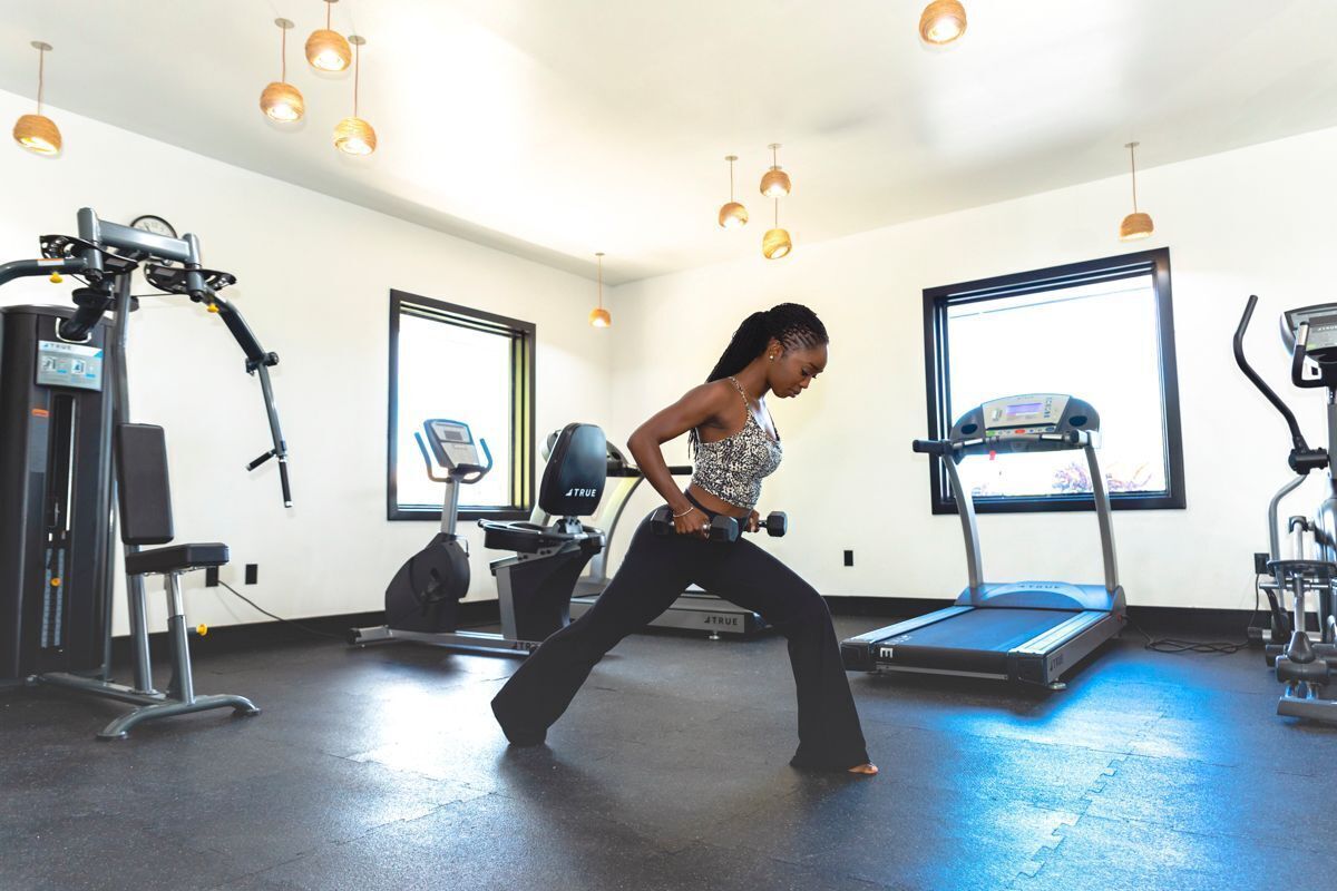 Une salle de sport équipée de matériel d’exercice, d’un tapis de course et d’une personne qui fait des étirements.