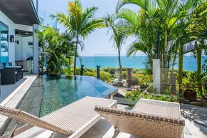 A modern pool area with lounge chairs, a glass barrier, and a view of the ocean. - Tamarind Hills Resort - Oasis (Antigua and Barbuda)