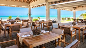 Een terras met houten tafels en stoelen met uitzicht op een strand.