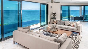 A modern living room with a large sofa, a coffee table, and a view of the ocean through floor-to-ceiling glass doors. - Tamarind Hills Resort - Ocean Blue (Antigua and Barbuda)