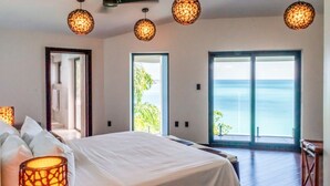 A bedroom with a large bed, a view of the ocean through a sliding door, and decorative hanging lamps. - Tamarind Hills Resort - Ocean Blue (Antigua and Barbuda)