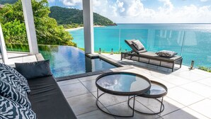 A luxurious outdoor area with a glass infinity pool, a lounge chair, and a round table. - Tamarind Hills Resort - Ocean Blue (Antigua and Barbuda)