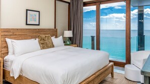 A bedroom with a large bed, a nightstand, a lamp, and a view of the ocean through a sliding glass door. - Tamarind Hills Resort - Barracuda 8 (Antigua and Barbuda)