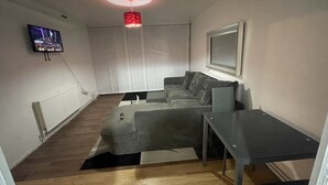 A modern living room with a grey sofa, a small table, and a TV mounted on the wall. - New! Xtra Large 4 Bedroom Up to 14 Guests (London)